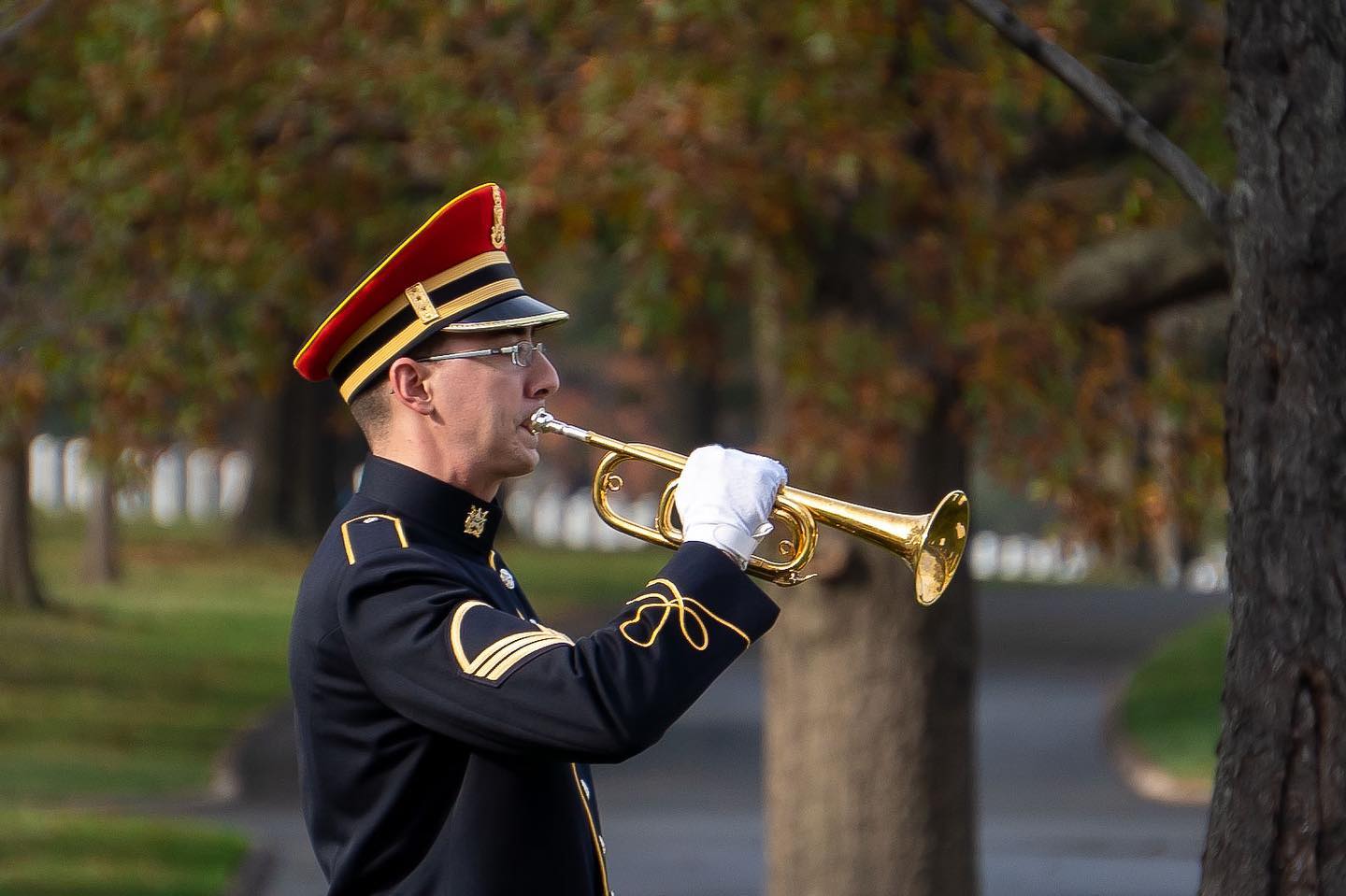 A bugler plays Taps at a full honors service in section 67 of Arlington National Cemetery as the leaves changed last week.

This bugler is part of the US Army Band, "Pershings Own". With America’s entrance into World War I and the mobilization of a huge force, there arose a further need for music in the military to provide for ceremonies, parades, concerts, and for the general morale of troops. 

Today, the US Army Band’s mission is to “provide music throughout the spectrum of military operations, to instill in our soldiers the will to fight and win, foster the support of our citizens, and promote our national interests at home and abroad.

One of these missions is to honor veterans through the playing of Taps at military funerals here at Arlington.