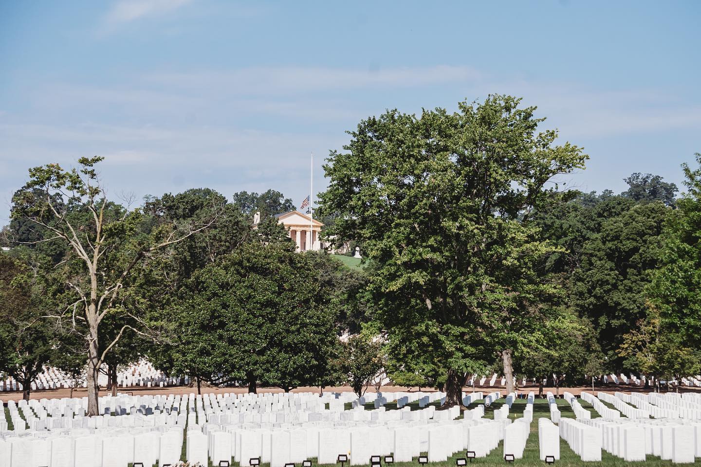 Rising above the cemetery is a huge mansion.  This is the Arlington House.

Arlington National Cemetery was established by Brigadier General Montgomery C. Meigs, who commanded the garrison at Arlington House, appropriated the grounds in 1864, for use as a military cemetery. His intention was to render the house uninhabitable should the Lee family ever attempt to return. 

A stone and masonry burial vault in the rose garden, 20 feet wide and 10 feet deep, and containing the remains of 1,800 Bull Run casualties, was among the first monuments to Union dead erected under Meigs' orders. Meigs himself was later buried within 100 yards of Arlington House with his wife, father and son; the final statement to his original order.

Neither Robert E. Lee, nor his wife, as title holder, ever attempted to publicly recover control of Arlington House. They were buried at Washington University (later renamed Washington and Lee University) where Lee had served as president. The couple never returned to the home George Washington Parke Custis had built and treasured.

Today this house watches over the ceremony and stands in honor over each and every soldier and veteran buried on those hallowed grounds.