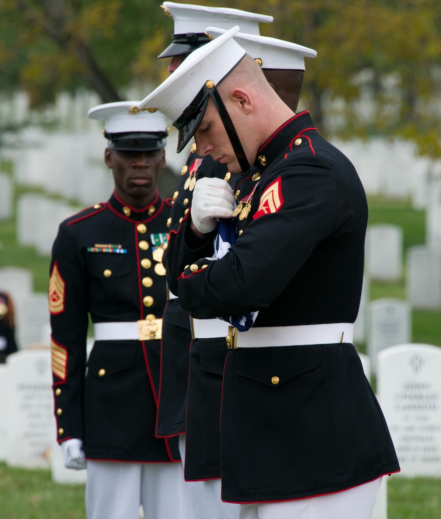 A member of the United States Marine Honor Guard inspects a carefully folded flag before passing it along at a military funeral at Arlington National Cemetery in Arlington, Virginia.