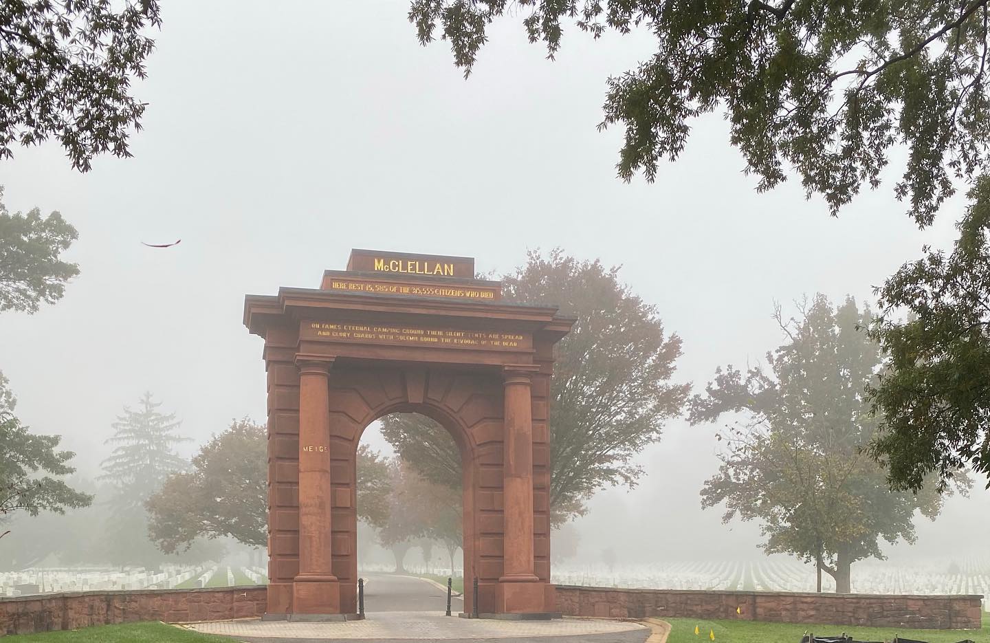 McClellan Gate can be seen standing erect amidst the early morning fog at Arlington National Cemetery in Arlington, Virginia. 

McClellan Gate marks the original entrance to Arlington National Cemetery. Named for Civil War General George B. McClellan, the reddish-brown archway remains one of the cemetery's most iconic landmarks, towering 30 feet above the ground. Atop the arch facing east, the name "McClellan" is inscribed in gold, above lines from Theodore O'Hara's poem 

“Bivouac of the Dead" (1847): 

“On fame's eternal camping ground their silent tents are spread / And glory guards with solemn round, the bivouac of the dead." Other lines from the poem are on the west-facing arch: "Rest on embalmed and sainted dead, dear as the blood ye gave / No impious footsteps here shall tread on the herbage of your grave." 

Like McClellan, O'Hara fought in the Mexican-American War (1846-1848) and wrote the poem to honor fallen soldiers from that conflict. However, "Bivouac of the Dead" became most closely associated with the Civil War, as it appeared on both Union and Confederate monuments during the 1860s.