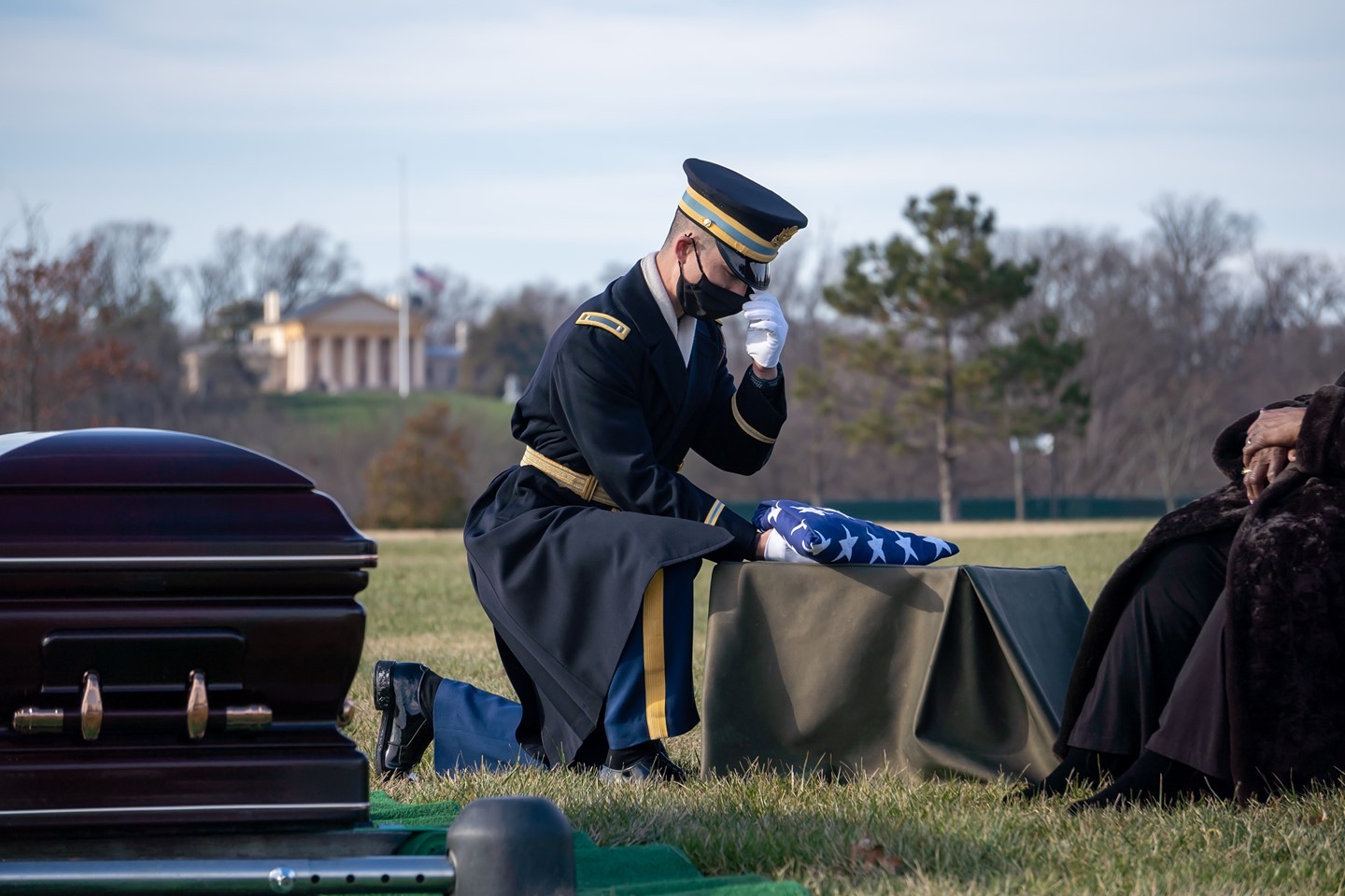A member of The Old Guard presents a flag during a service honoring a veteran at Arlington National Cemetery in Arlington, Virginia.

The Arlington House can be seen in the late afternoon sun from Section 57 in the background.