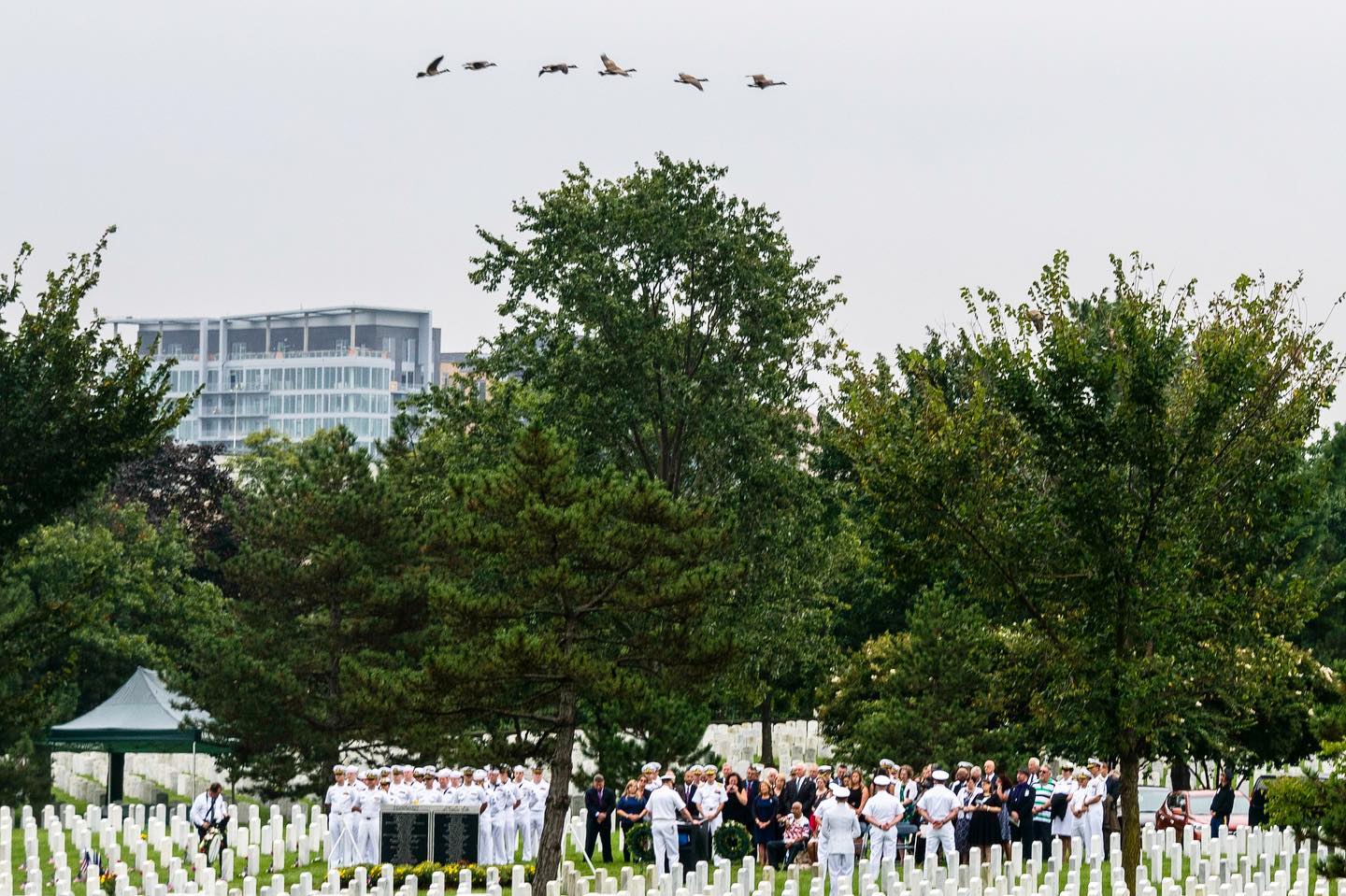 Geese fly over a service in Section 64 of Arlington National Cemetery. To the left of the image can be seen the Pentagon Group Burial Marker, which honors and commemorates those lives lost during the 9/11 attack on the Pentagon. 

The monument is inscribed with 184 names, honoring all those that perished in the Pentagon and on American Airlines Flight 77.

The monument is located off Patton Circle in Section 64, in the southeastern part of the cemetery, closest to the Pentagon.

We will never forget.